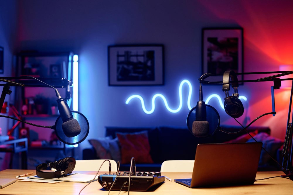 Vue de face de deux micros avec filtres anti-pop et une console de mixage dans un studio de podcast éclairé par des néons bleus et roses