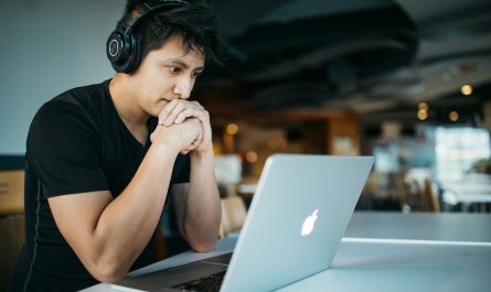 man wearing headphones while sitting on chair in front of MacBook
