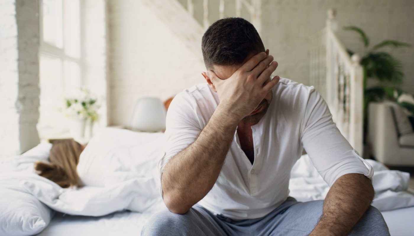 Man sitting on bed with hand over face