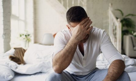 Man sitting on bed with hand over face