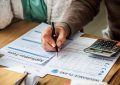 Personne remplissant un formulaire d'assurance avec une calculatrice pour vérifier les montants TTC et la TVA.