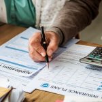 Personne remplissant un formulaire d'assurance avec une calculatrice pour vérifier les montants TTC et la TVA.
