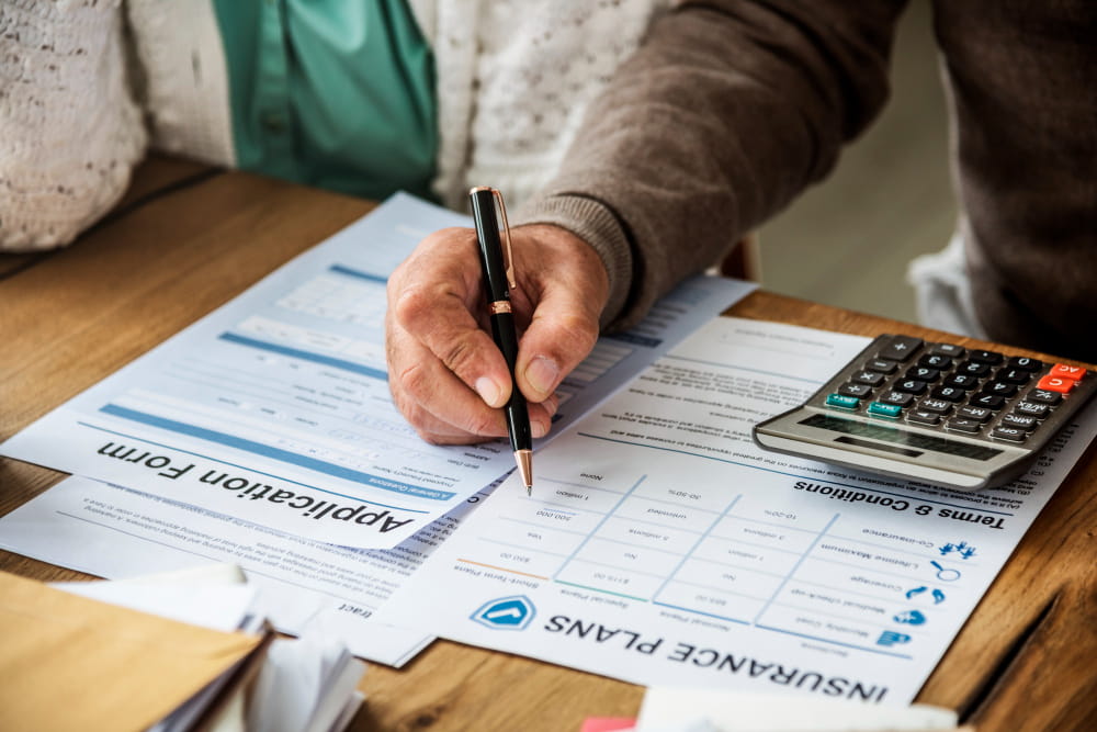Personne remplissant un formulaire d'assurance avec une calculatrice pour vérifier les montants TTC et la TVA.