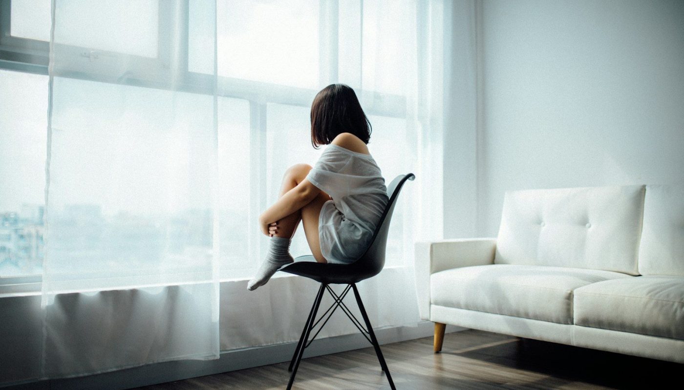 woman sitting on black chair in front of glass-panel window with white curtains