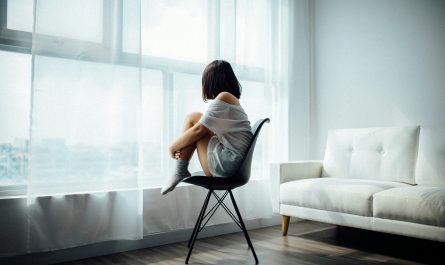 woman sitting on black chair in front of glass-panel window with white curtains