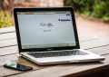 Laptop ouvert sur Google, smartphone à gauche, table en bois, jardin flou