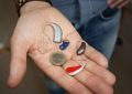 Une main montre plusieurs aides auditives et une pièce de monnaie