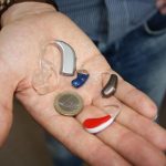 Une main montre plusieurs aides auditives et une pièce de monnaie