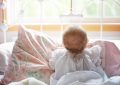 Un bébé assis sur un lit, regardant par la fenêtre