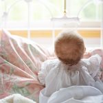 Un bébé assis sur un lit, regardant par la fenêtre