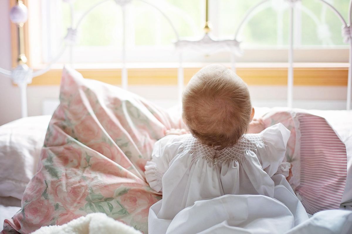 Un bébé assis sur un lit, regardant par la fenêtre