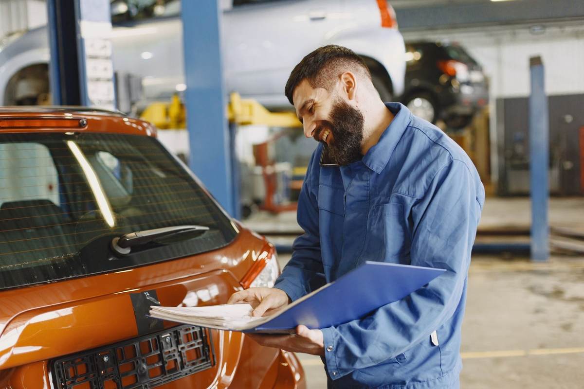 Mécanicien avec un véhicule rouge en garage, feuille de travail