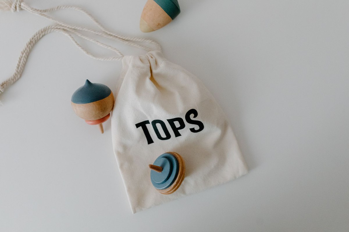 Un sac à dessin blanc contenant trois toupies colorées sur fond blanc